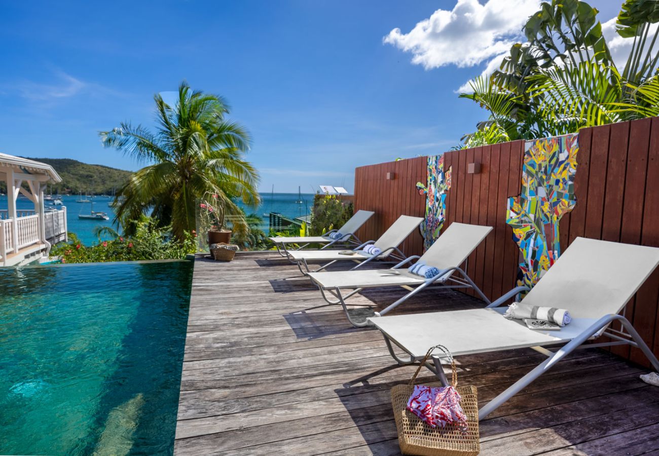 Grey sun loungers on a wooden deck, infinity pool and panoramic sea views in Anses-d'Arlet.