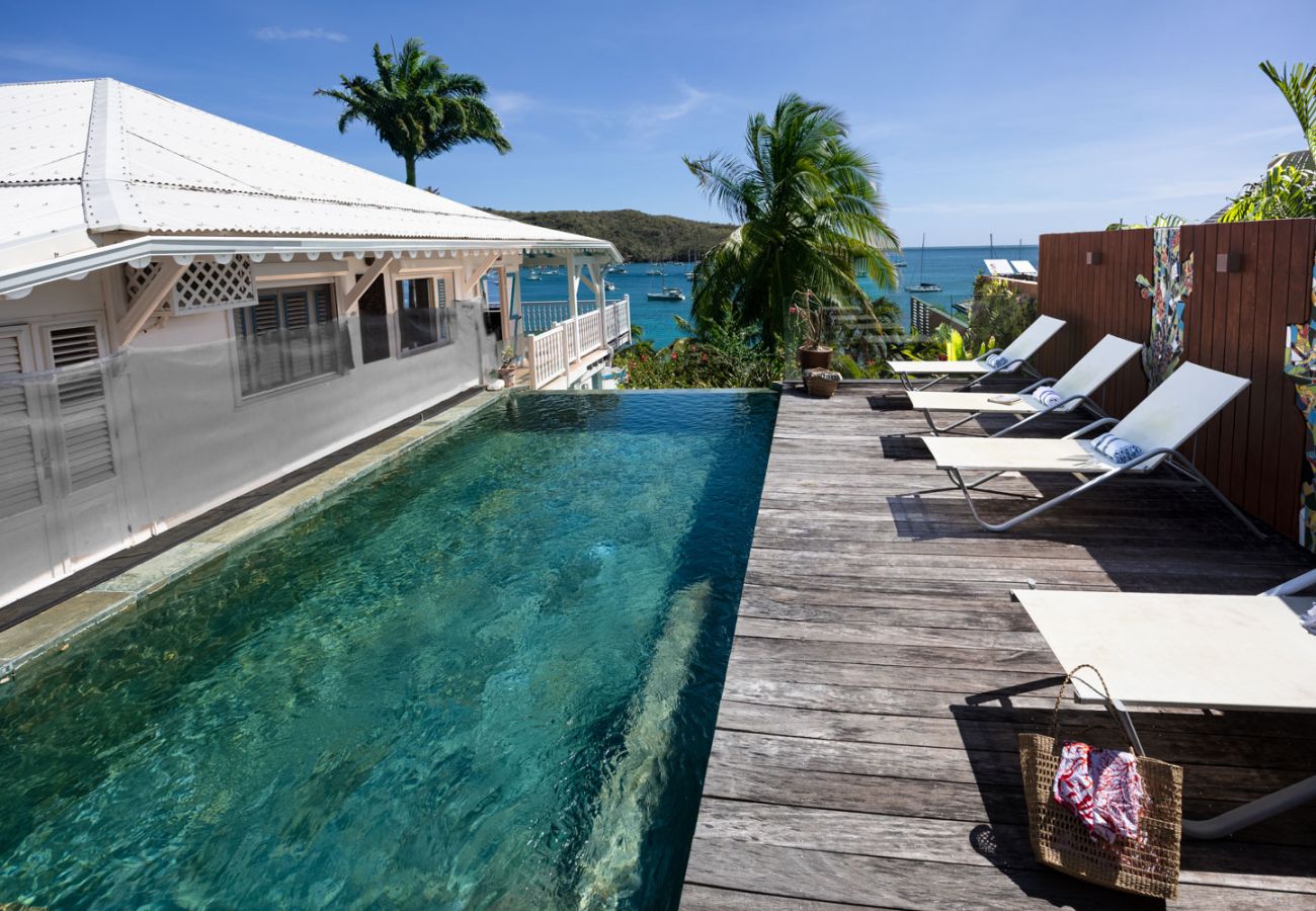 Piscine à débordement turquoise et deck en bois avec transats face à la mer aux Anses-d'Arlet, Martinique.