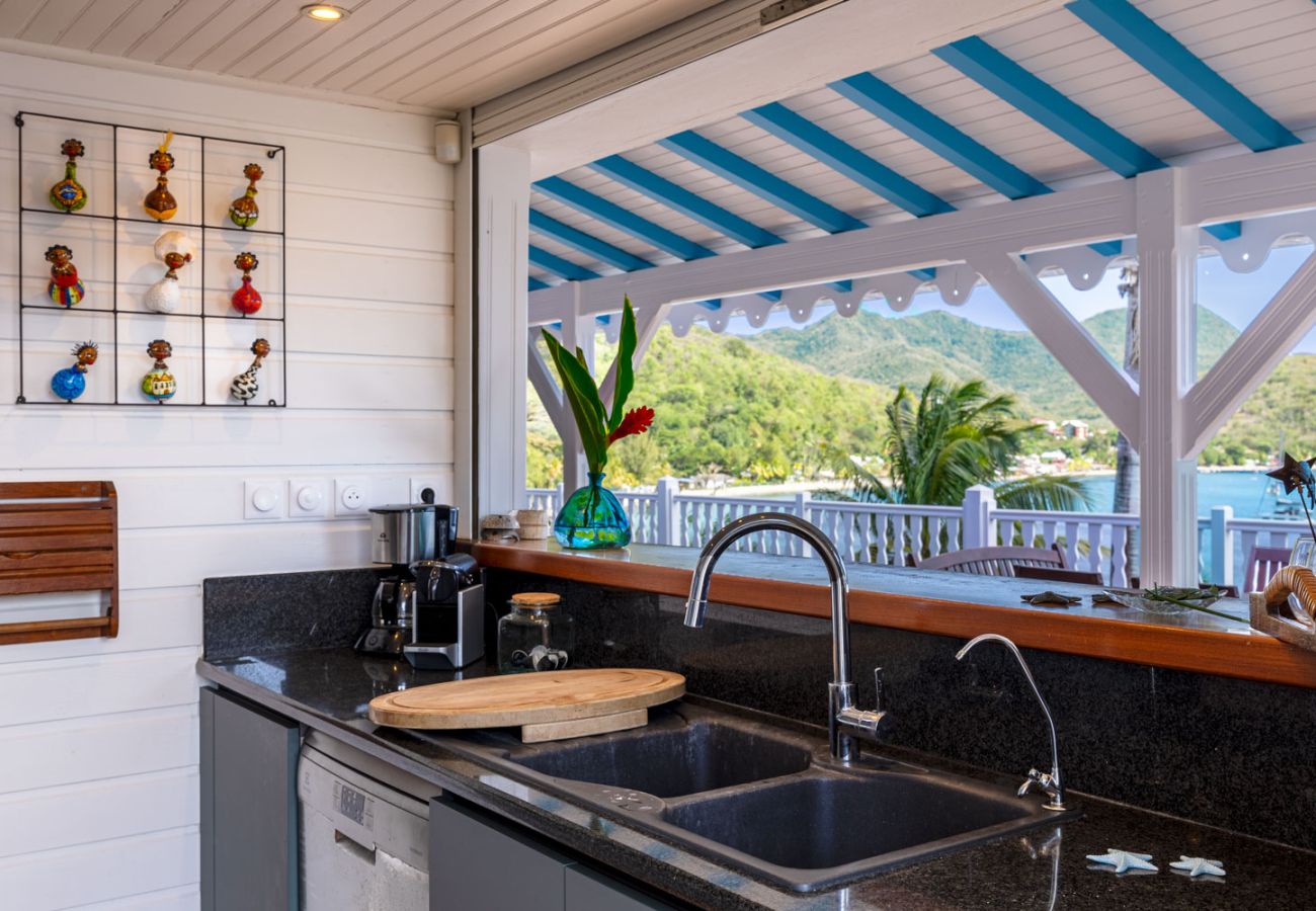 Cuisine équipée avec plan de travail sombre, évier double et large ouverture sur la baie des Anses-d'Arlet en Martinique.