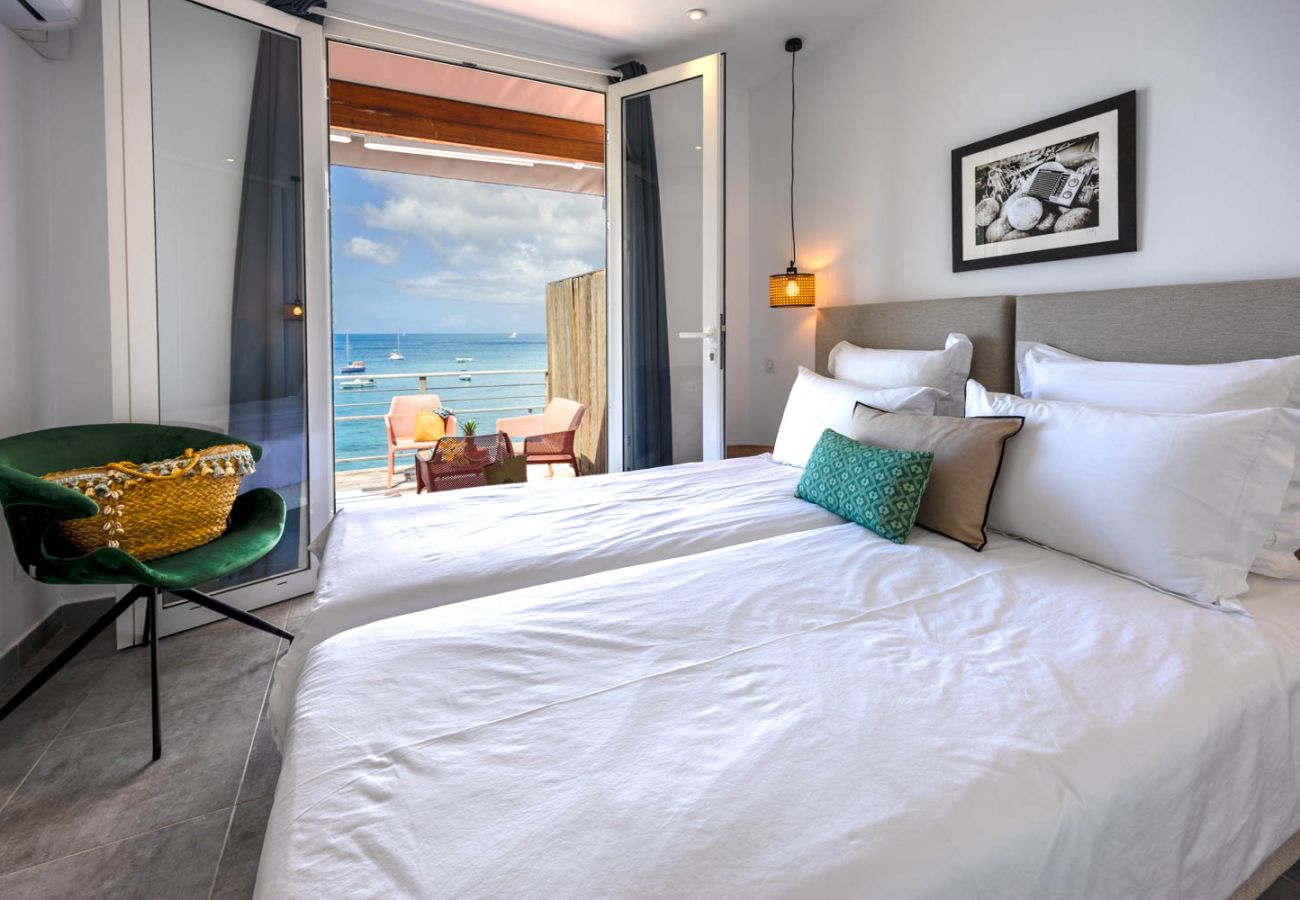 Chambre parentale lumineuse, lit king size, fauteuil vert et porte-fenêtre ouvrant sur la mer aux Anses-d'Arlet.