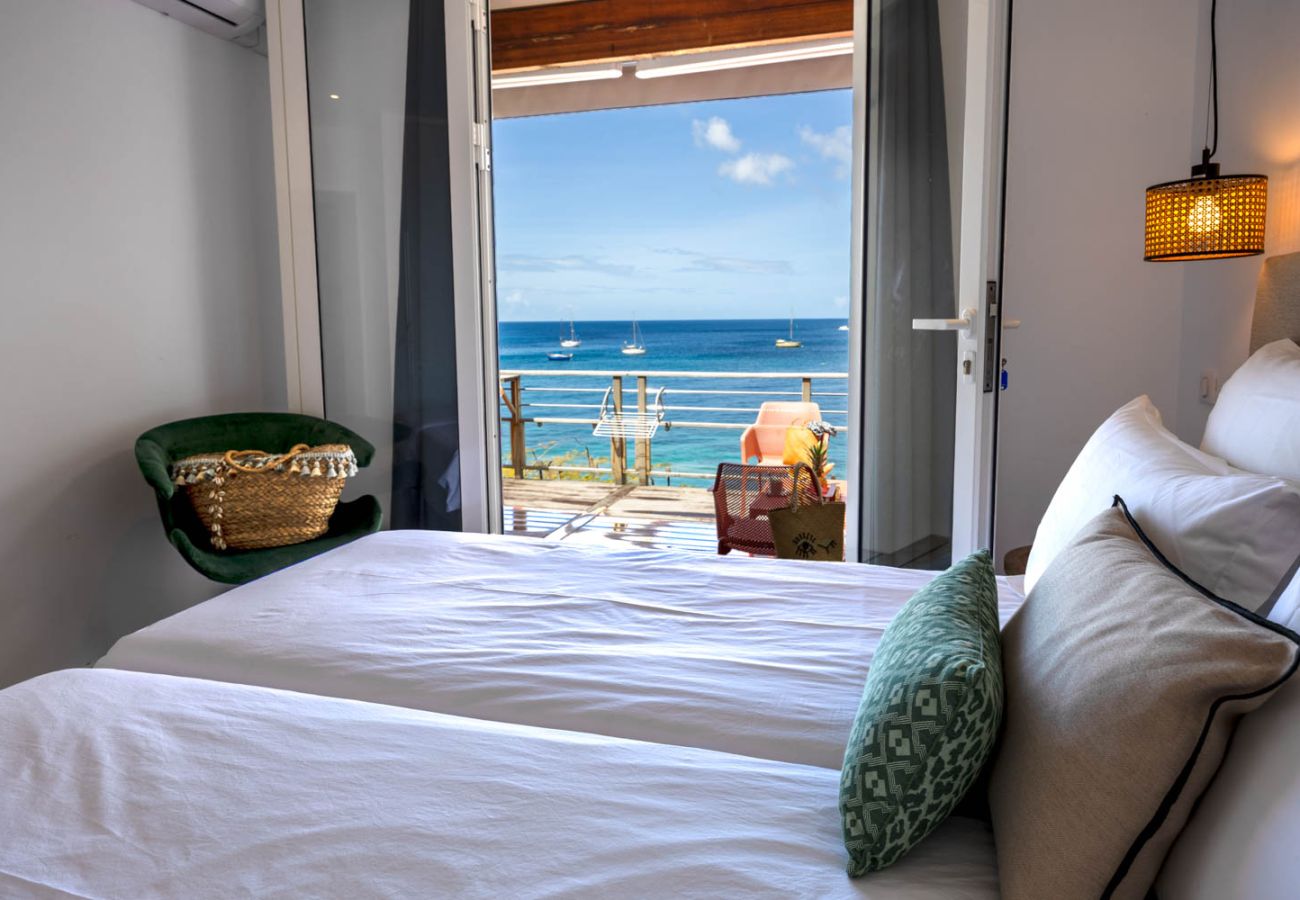 Chambre lumineuse de l'appartement Ti Soleil avec vue directe sur la mer et les bateaux depuis le lit, aux Anses-d'Arlet.