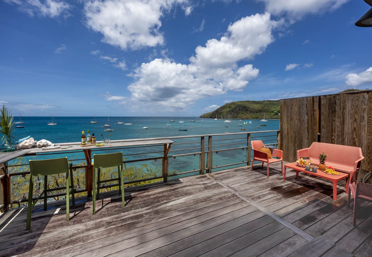 Terrasse en bois avec coin salon, fauteuils et bar face à la mer et aux bateaux aux Anses-d'Arlet.