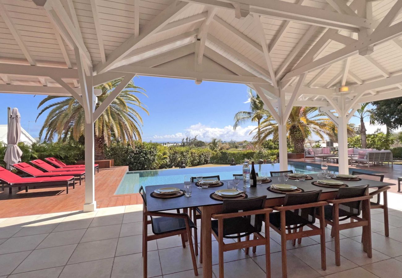 Table de repas sous la terrasse couverte avec vue sur la piscine et le jardin de la Villa Sol à Saint-François